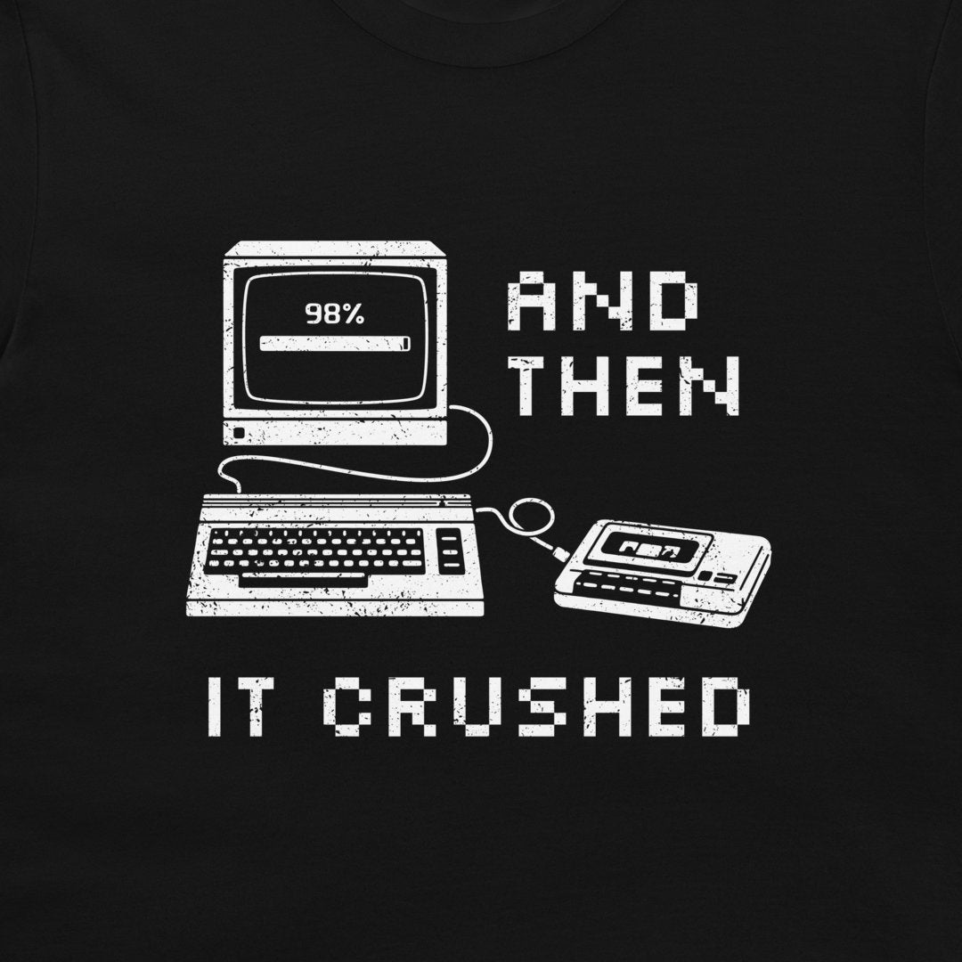 A black t-shirt featuring a white distressed graphic of retro computer hardware (monitor, keyboard, cassette tape) with pixelated text reading 'AND THEN IT CRUSHED'.