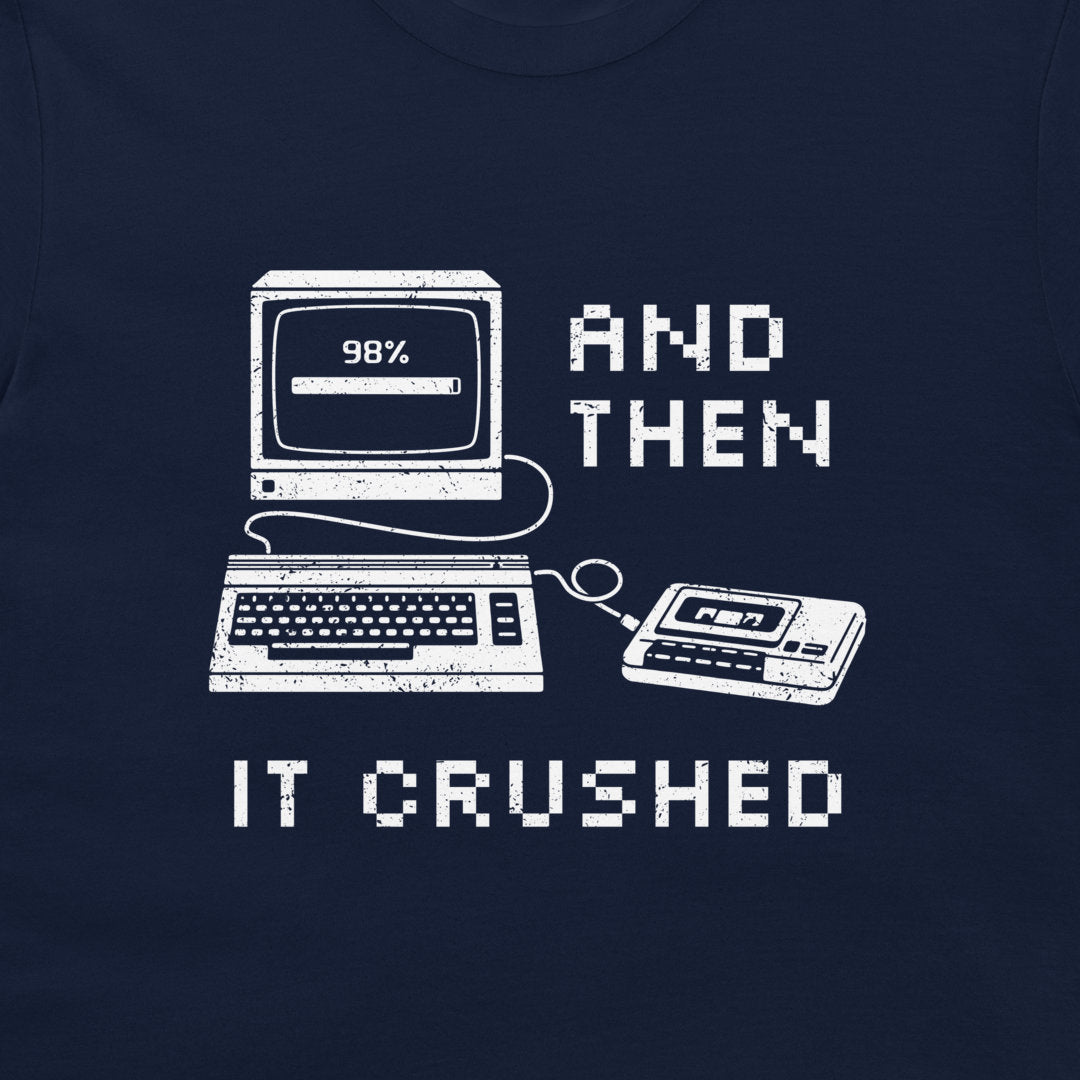 A close-up of a navy blue t-shirt, featuring a white distressed graphic of retro computer technology with the text 'AND THEN IT CRUSHED'.