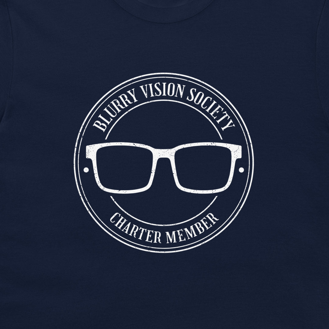 A close-up of a navy blue t-shirt, featuring a distressed white circular graphic that reads 'BLURRY VISION SOCIETY CHARTER MEMBER' around a pair of glasses.