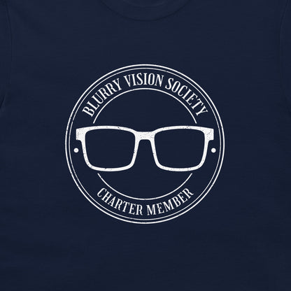 A close-up of a navy blue t-shirt, featuring a distressed white circular graphic that reads 'BLURRY VISION SOCIETY CHARTER MEMBER' around a pair of glasses.