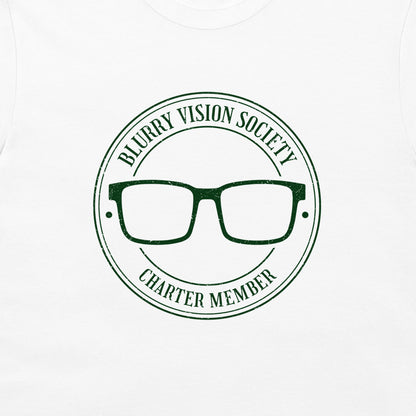 A close-up of a white t-shirt, featuring a dark green circular graphic print that reads 'BLURRY VISION SOCIETY CHARTER MEMBER' around a pair of glasses.