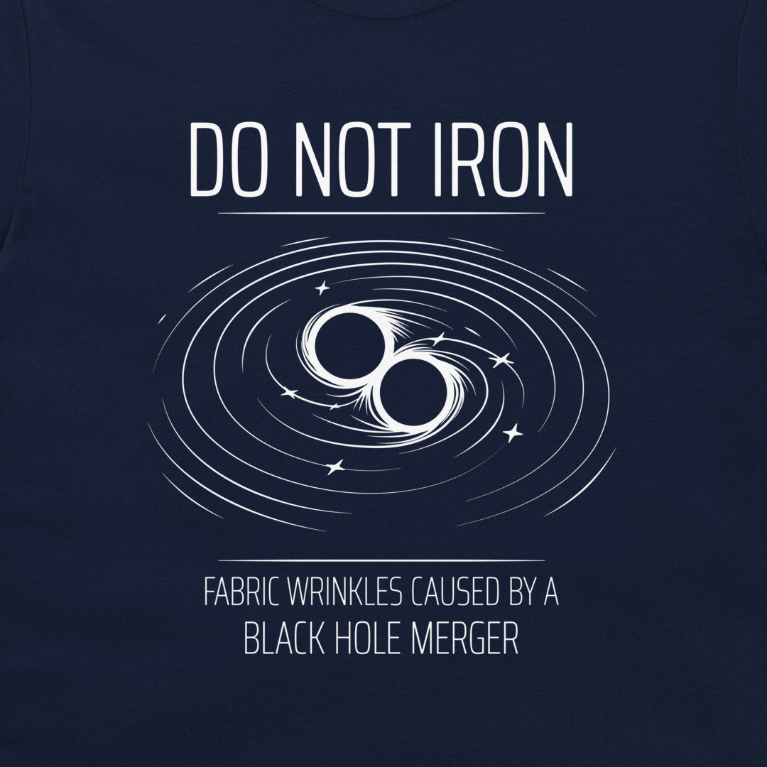 A close-up of a navy blue t-shirt, featuring a white graphic print of a black hole merger with the text 'DO NOT IRON' and 'FABRIC WRINKLES CAUSED BY A BLACK HOLE MERGER'.