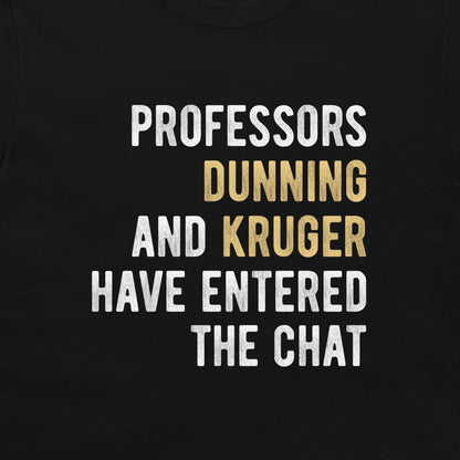 A close-up of a black t-shirt featuring a humorous text graphic printed in white and gold. The text reads 'PROFESSORS DUNNING AND KRUGER HAVE ENTERED THE CHAT'.