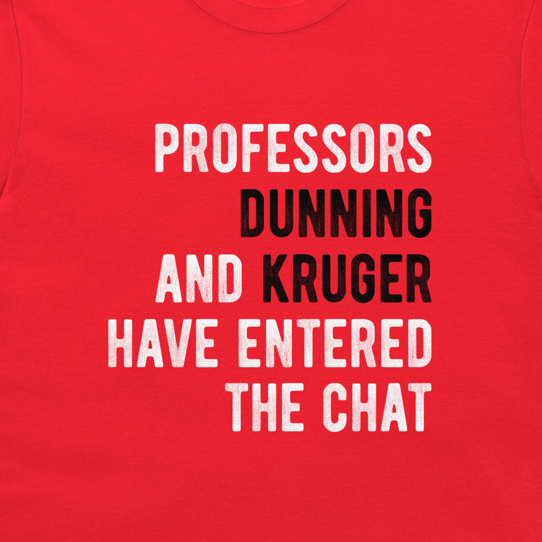 A close-up of a red t-shirt featuring a humorous text graphic printed in white and black block letters that reads 'PROFESSORS DUNNING AND KRUGER HAVE ENTERED THE CHAT'.