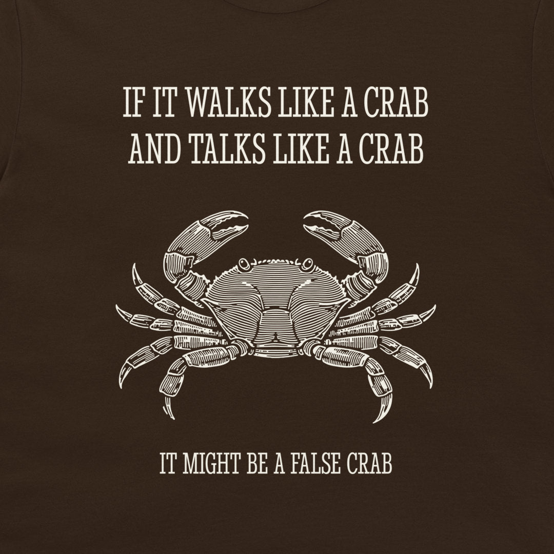 A dark brown graphic print on a t-shirt featuring a white line art illustration of a crab and the humorous text 'IF IT WALKS LIKE A CRAB AND TALKS LIKE A CRAB IT MIGHT BE A FALSE CRAB'.