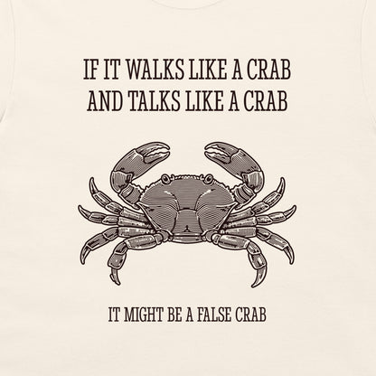 A close-up of a cream-colored garment, likely a t-shirt, featuring a black graphic print of a crab and the humorous text 'IF IT WALKS LIKE A CRAB AND TALKS LIKE A CRAB IT MIGHT BE A FALSE CRAB'.