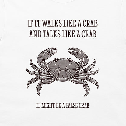 A white graphic t-shirt featuring a black line art illustration of a crab with the humorous text 'IF IT WALKS LIKE A CRAB AND TALKS LIKE A CRAB IT MIGHT BE A FALSE CRAB'.