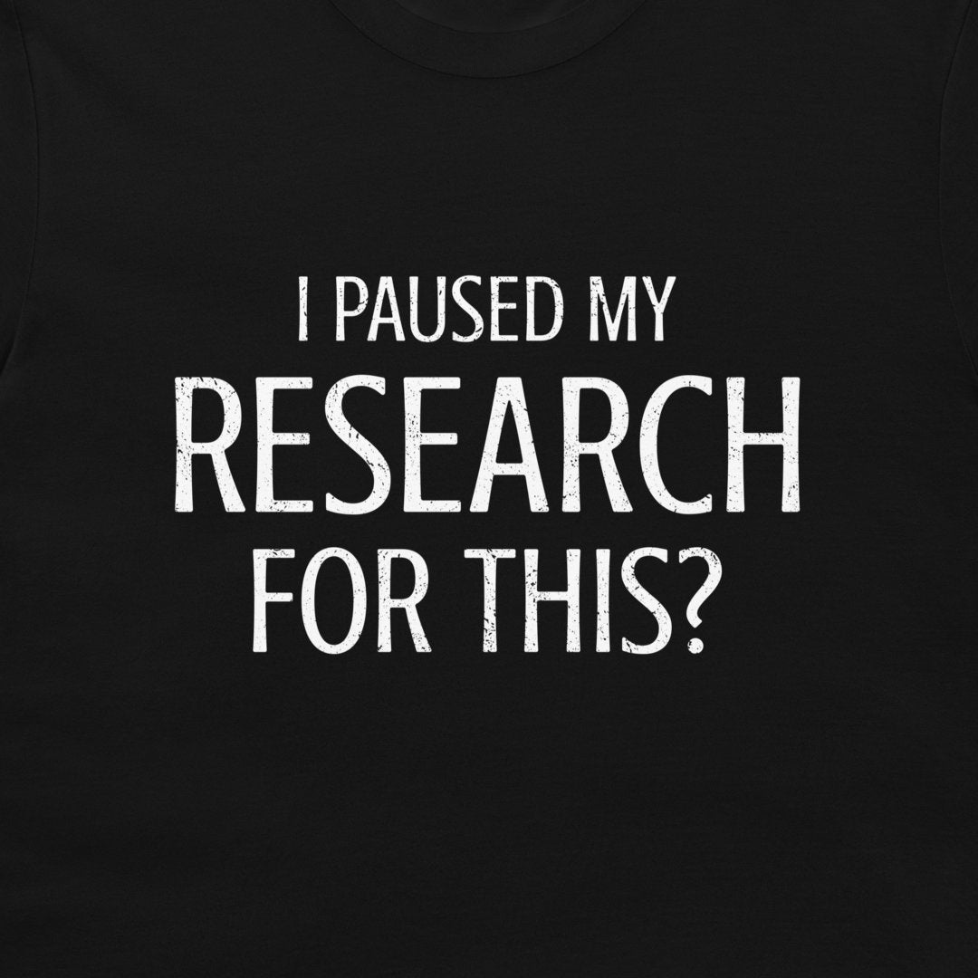 A close-up of a black t-shirt featuring the text 'I PAUSED MY RESEARCH FOR THIS?' printed in a distressed white sans-serif font.