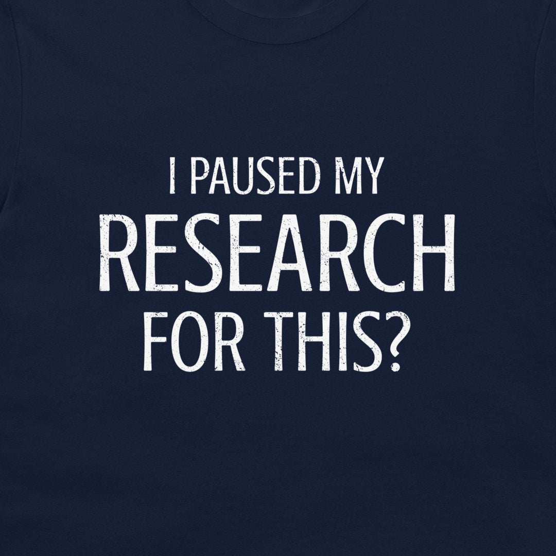 A close-up of a navy blue t-shirt featuring a distressed white text graphic that reads 'I PAUSED MY RESEARCH FOR THIS?'.
