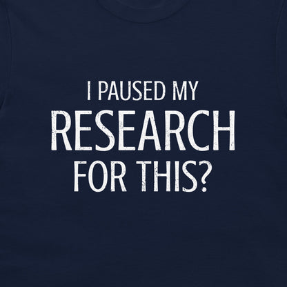 A close-up of a navy blue t-shirt featuring a distressed white text graphic that reads 'I PAUSED MY RESEARCH FOR THIS?'.