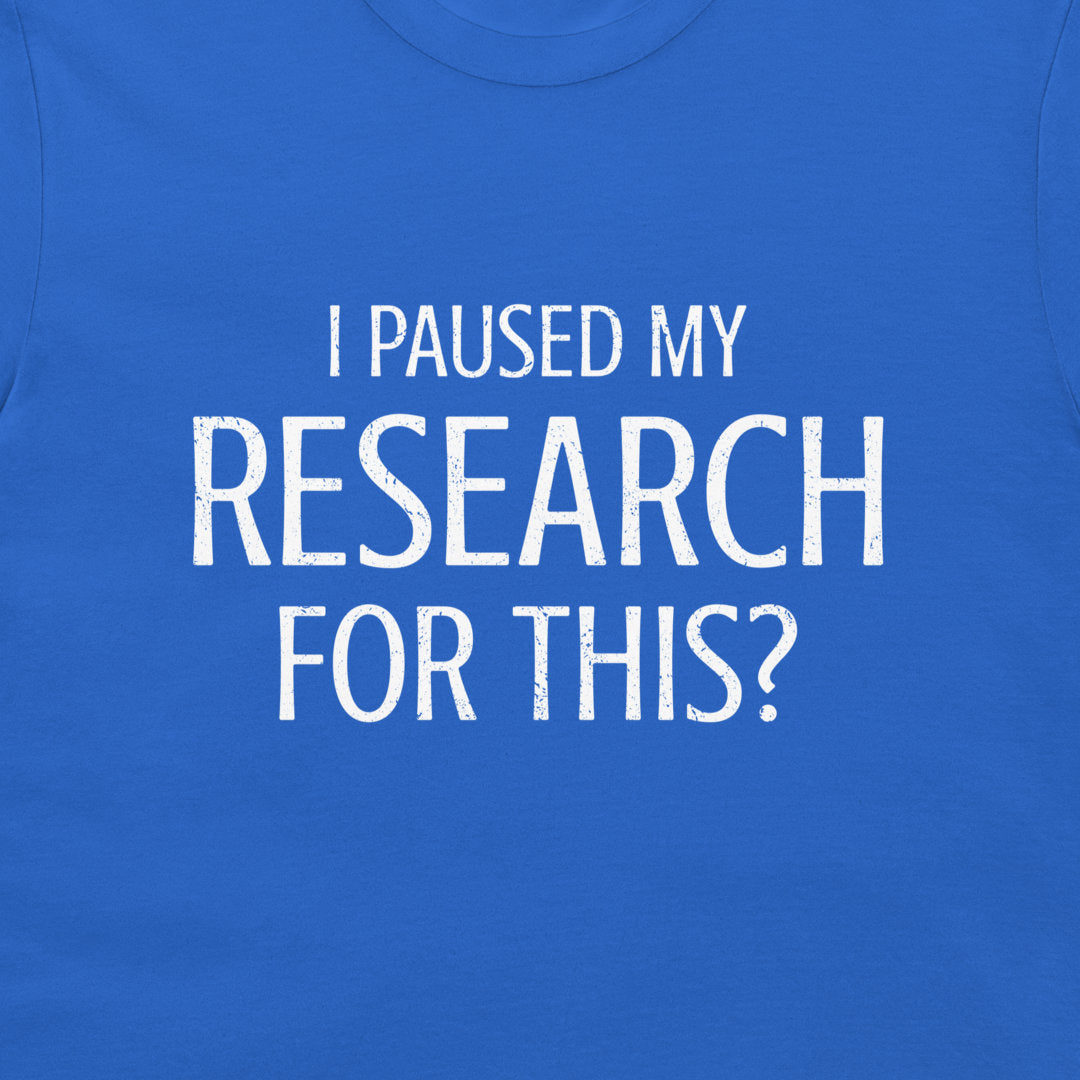 A close-up of a royal blue t-shirt featuring the text 'I PAUSED MY RESEARCH FOR THIS?' printed in a distressed white sans-serif font across the chest.