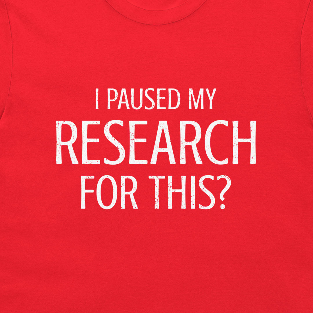 A close-up of a bright red t-shirt featuring the text 'I PAUSED MY RESEARCH FOR THIS?' printed in a distressed white sans-serif font across the chest.