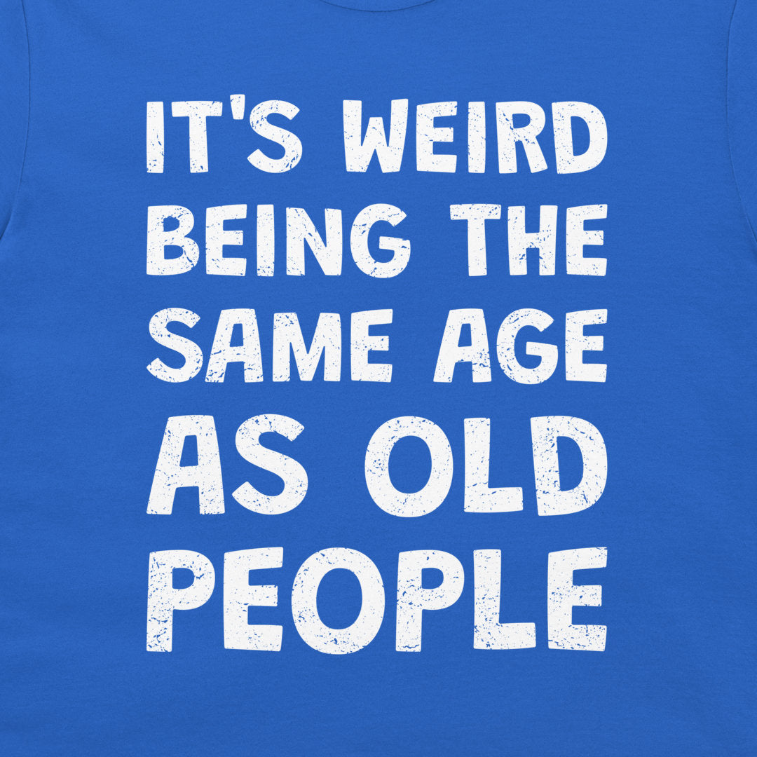 A close-up of a blue T-shirt with large distressed white text reading 'IT'S WEIRD BEING THE SAME AGE AS OLD PEOPLE'.