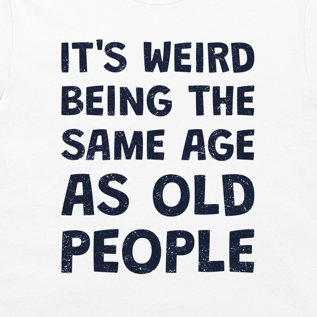 White t-shirt with a dark navy blue distressed text graphic that reads 'IT'S WEIRD BEING THE SAME AGE AS OLD PEOPLE'.