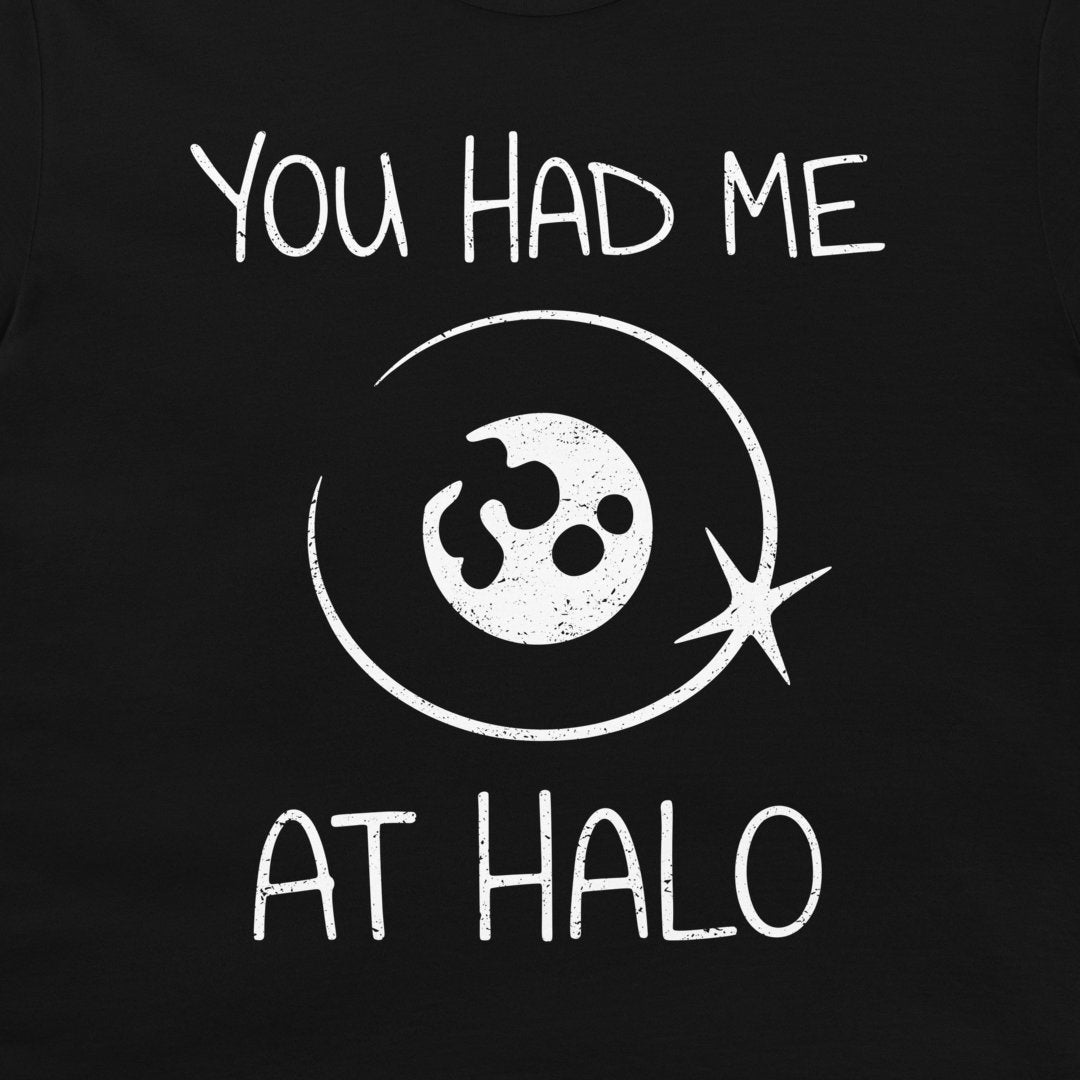 A close-up of a black t-shirt, featuring a distressed white graphic print that reads 'YOU HAD ME AT HALO' around a stylized moon with a halo around.