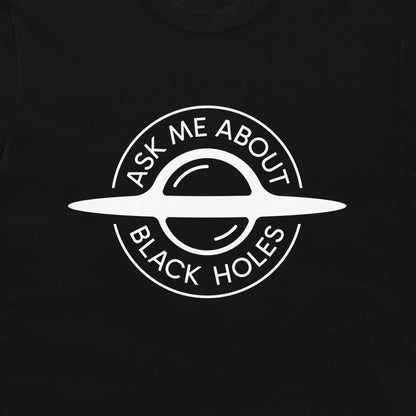 A close-up of a black t-shirt, featuring a white circular graphic of a ringed black hole with the text 'ASK ME ABOUT BLACK HOLES' printed on the chest.