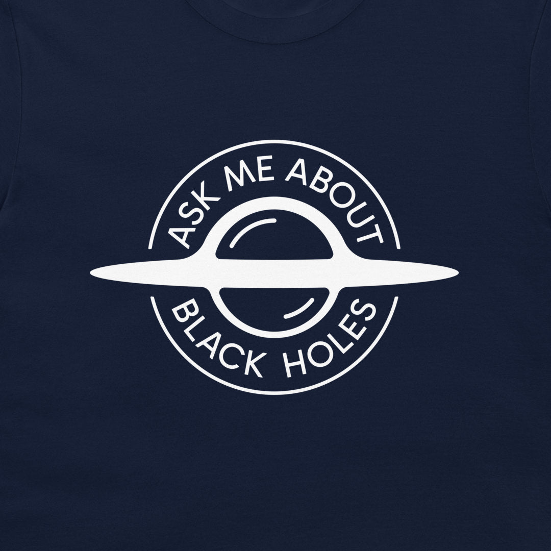 A close-up of a navy blue t-shirt featuring a white circular graphic of a ringed black hole with the text 'ASK ME ABOUT BLACK HOLES' printed on the front.