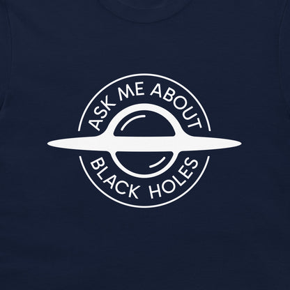 A close-up of a navy blue t-shirt featuring a white circular graphic of a ringed black hole with the text 'ASK ME ABOUT BLACK HOLES' printed on the front.