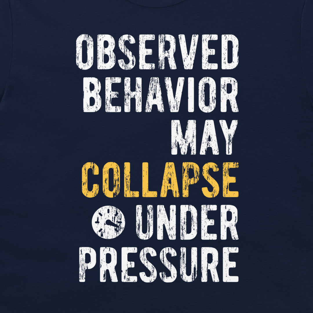 A close-up of a navy blue graphic t-shirt featuring distressed white and yellow text that reads 'OBSERVED BEHAVIOR MAY COLLAPSE UNDER PRESSURE'.