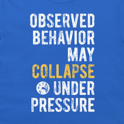 A close-up of a blue t-shirt featuring a distressed typographic graphic in white and yellow that reads, 'OBSERVED BEHAVIOR MAY COLLAPSE UNDER PRESSURE'.