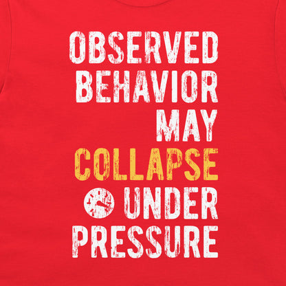 A close-up of a red shirt or fabric panel with large distressed white text reading 'OBSERVED BEHAVIOR MAY COLLAPSE UNDER PRESSURE' and a small clock icon, with 'COLLAPSE' highlighted in yellow.