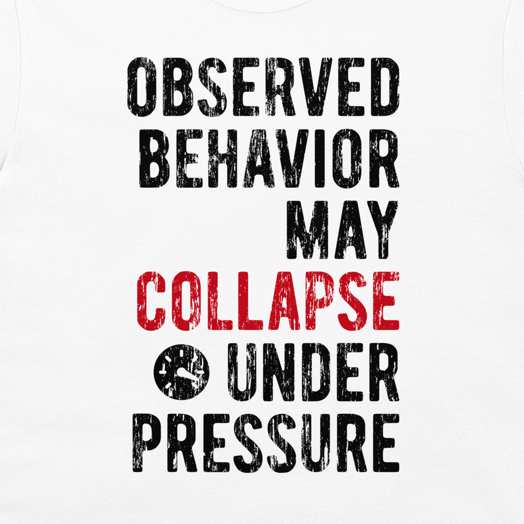 A close-up of a white t-shirt, featuring a distressed typographic print that reads 'OBSERVED BEHAVIOR MAY COLLAPSE UNDER PRESSURE' in black and red lettering.