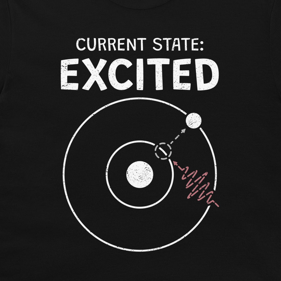 A close-up of a black T-shirt with a white graphic print that reads 'CURRENT STATE: EXCITED' above a simplified atom diagram and a photon wave line.