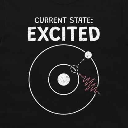 A close-up of a black T-shirt with a white graphic print that reads 'CURRENT STATE: EXCITED' above a simplified atom diagram and a photon wave line.