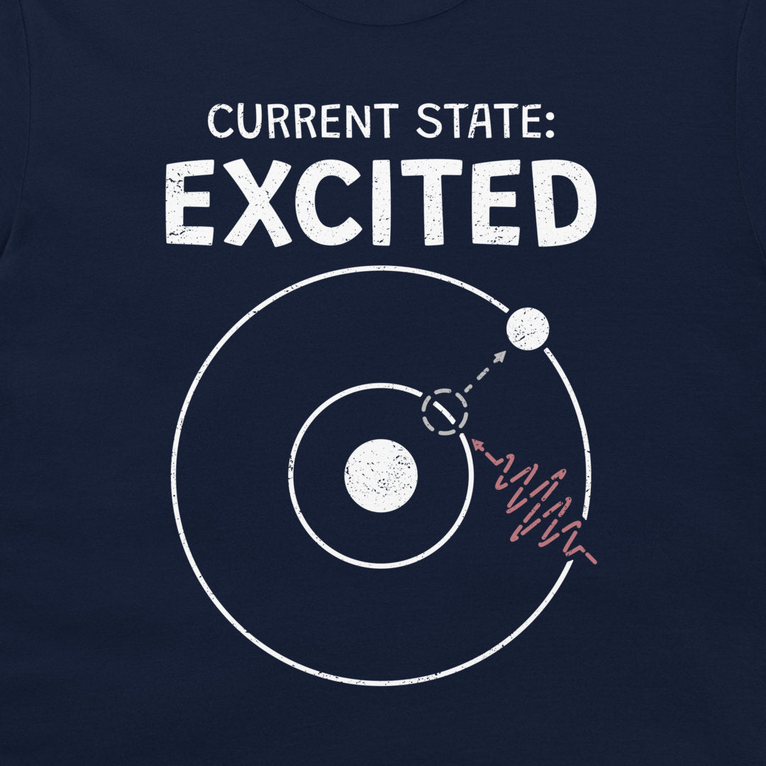 A close-up of a navy blue T-shirt with a white graphic print that reads 'CURRENT STATE: EXCITED' above a simplified atom diagram and a photon wave line.