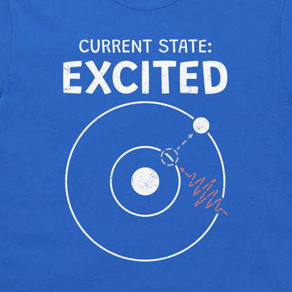 A close-up of a blue T-shirt with a white graphic print that reads 'CURRENT STATE: EXCITED' above a simplified atom diagram and a photon wave line.