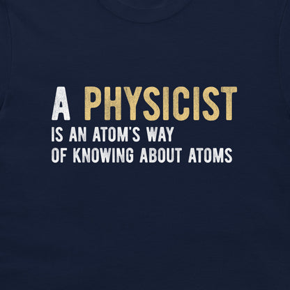 A close-up of a navy blue t-shirt featuring a printed graphic with the text 'A PHYSICIST IS AN ATOM'S WAY OF KNOWING ABOUT ATOMS' in white and gold lettering.