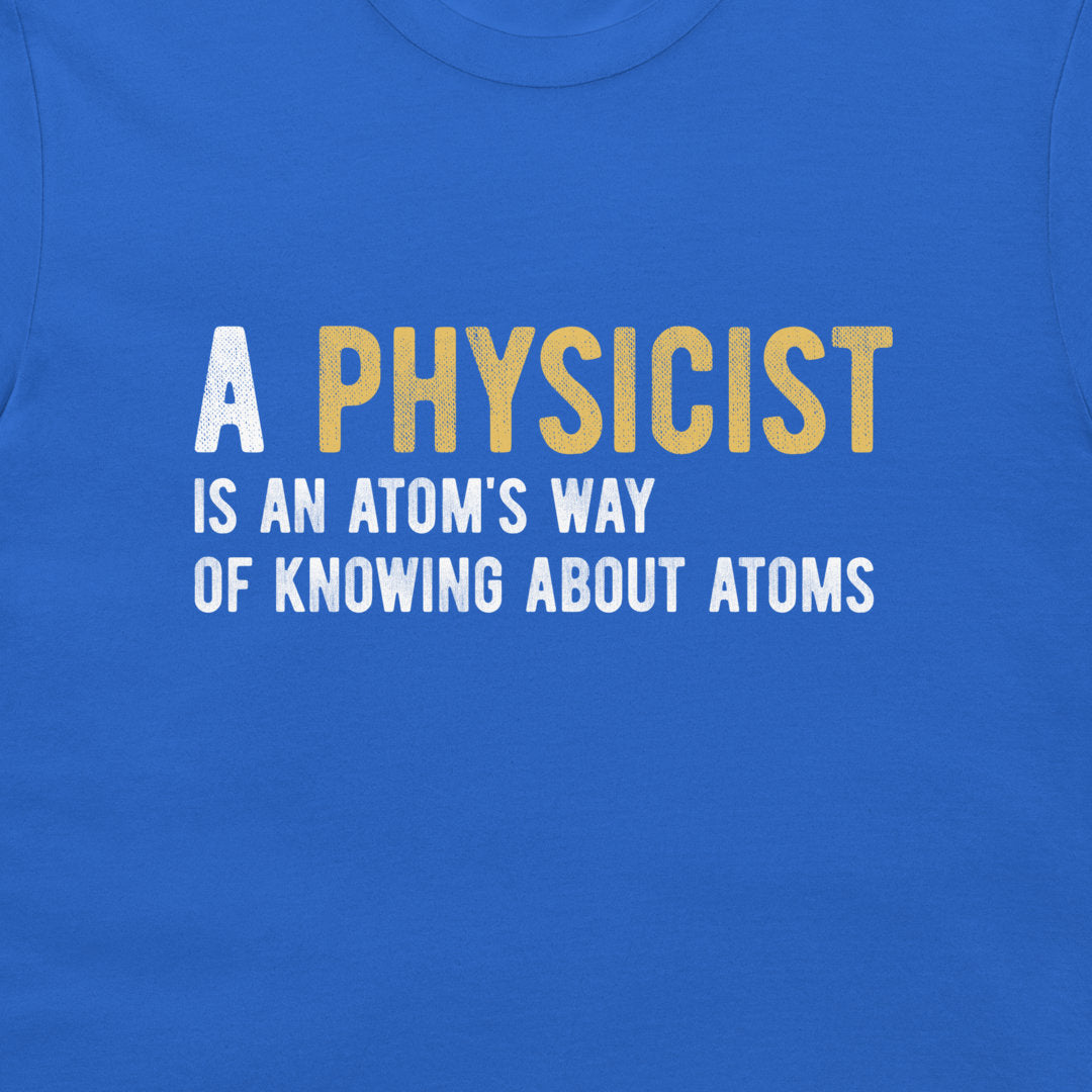 A close-up of a blue t-shirt featuring a printed graphic with the text 'A PHYSICIST IS AN ATOM'S WAY OF KNOWING ABOUT ATOMS' in white and yellow lettering.
