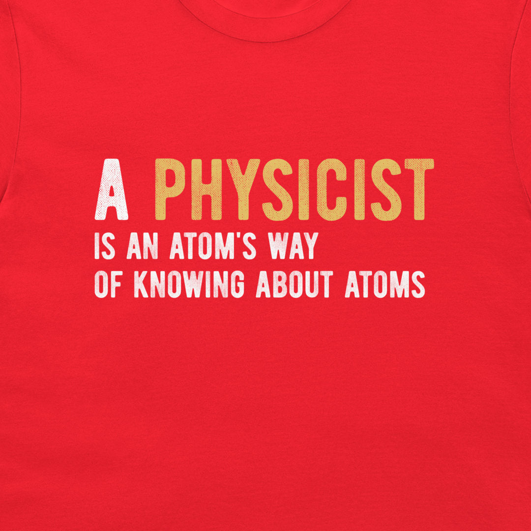 A close-up of a bright red t-shirt featuring a printed graphic with the text 'A PHYSICIST IS AN ATOM'S WAY OF KNOWING ABOUT ATOMS' in white and yellow lettering.