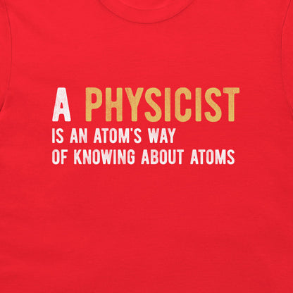 A close-up of a bright red t-shirt featuring a printed graphic with the text 'A PHYSICIST IS AN ATOM'S WAY OF KNOWING ABOUT ATOMS' in white and yellow lettering.