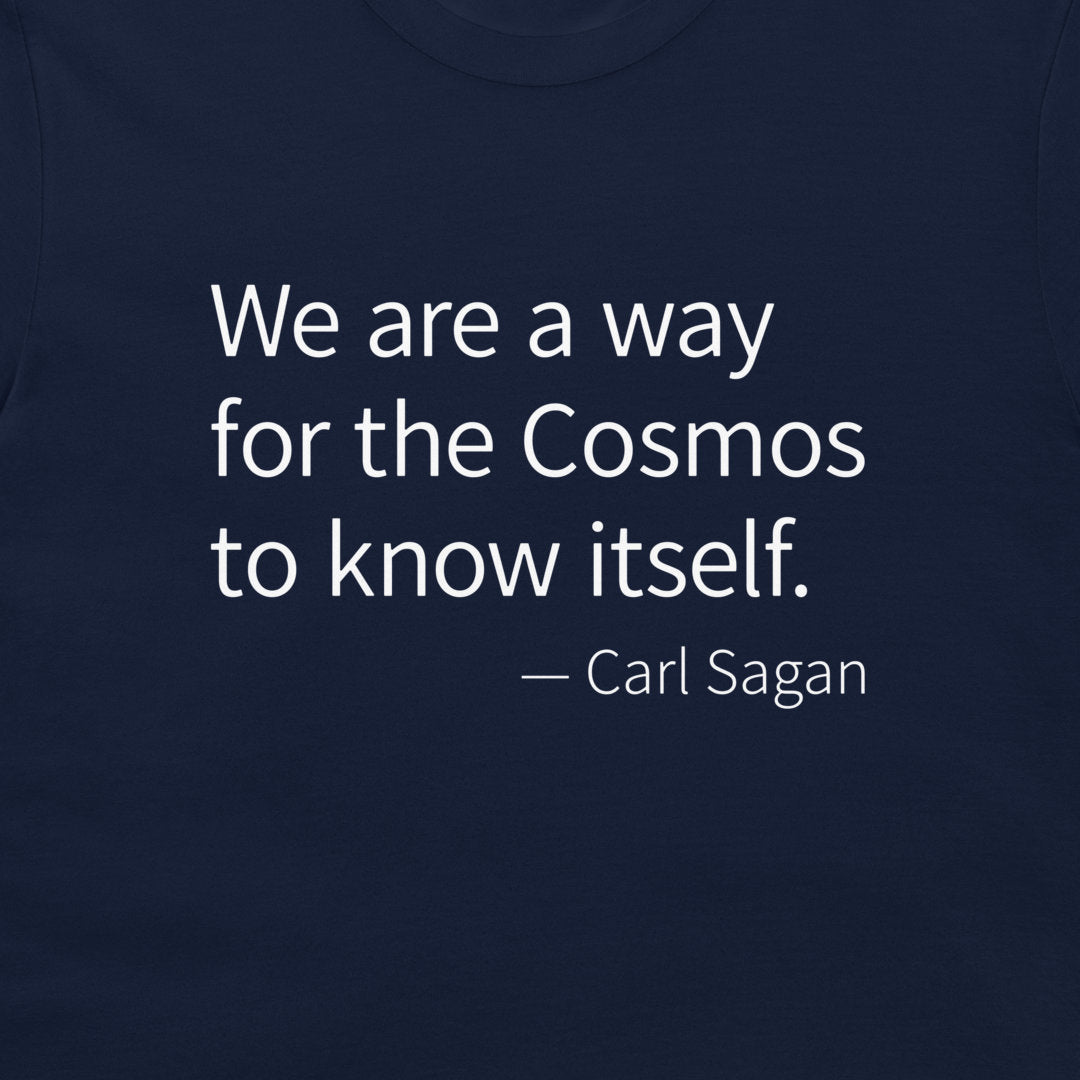 A close-up of a navy blue t-shirt featuring a white printed quote by Carl Sagan: 'We are a way for the Cosmos to know itself.'.