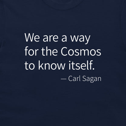 A close-up of a navy blue t-shirt featuring a white printed quote by Carl Sagan: 'We are a way for the Cosmos to know itself.'.