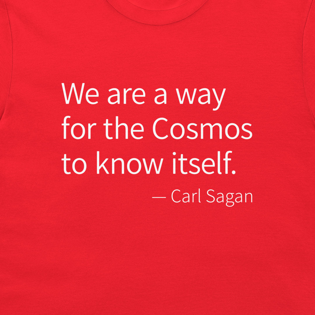 A close-up of a bright red t-shirt featuring a white printed quote by Carl Sagan: 'We are a way for the Cosmos to know itself.'.