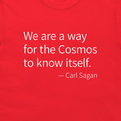 A close-up of a bright red t-shirt featuring a white printed quote by Carl Sagan: 'We are a way for the Cosmos to know itself.'.