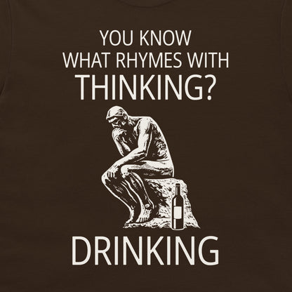 A dark brown t-shirt featuring a white graphic print of the Thinker statue next to a wine bottle, with the text 'YOU KNOW WHAT RHYMES WITH THINKING? DRINKING'.