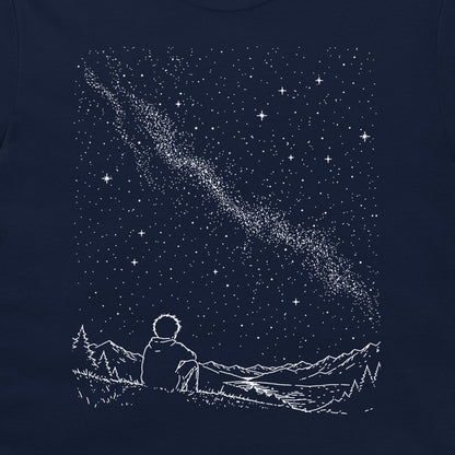 A dark navy blue t-shirt featuring a white line art graphic of a person sitting in a field of mountains, looking up at a starry night sky with a shooting star.