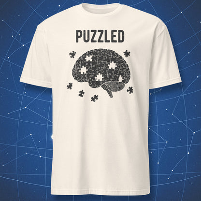 black puzzle brain design with scattered pieces and “Puzzled” text on natural shirt