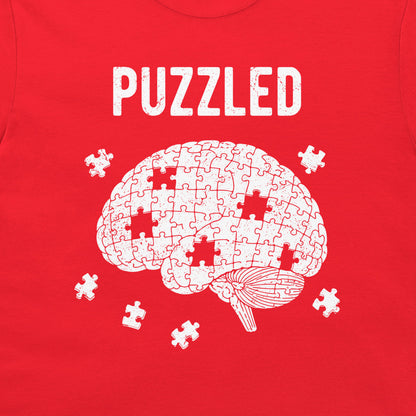 A red t-shirt featuring a white graphic of a brain made of puzzle pieces with several missing pieces scattered around it, and the word 'PUZZLED' printed above in a distressed white font.