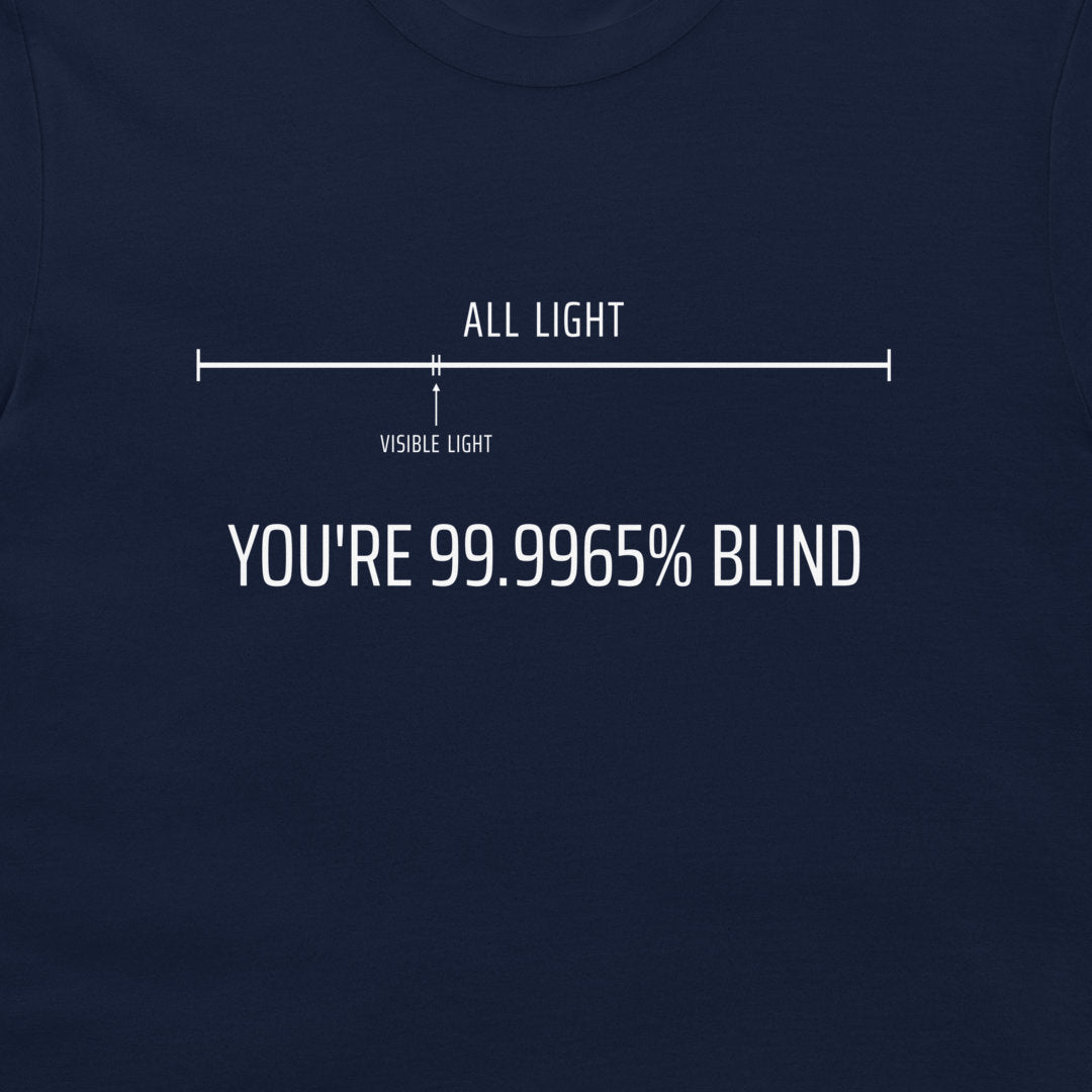 A close-up of a navy blue t-shirt featuring a white graphic print. The graphic shows a light bar diagram labeled 'ALL LIGHT' and 'VISIBLE LIGHT' with the text 'YOU'RE 99.9965% BLIND".