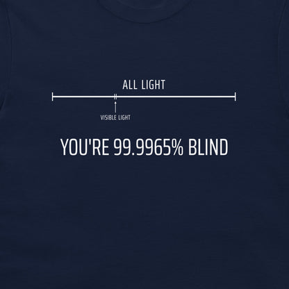 A close-up of a navy blue t-shirt featuring a white graphic print. The graphic shows a light bar diagram labeled 'ALL LIGHT' and 'VISIBLE LIGHT' with the text 'YOU'RE 99.9965% BLIND".