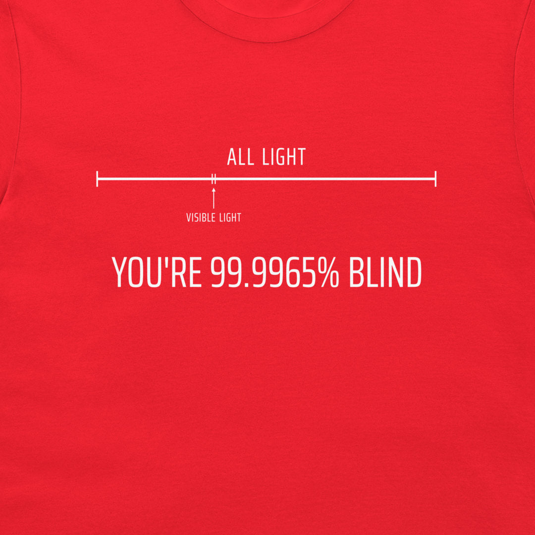 A close-up of a bright red t-shirt featuring a white graphic design. The design shows a horizontal line with 'ALL LIGHT' at the top and ''YOU'RE 99.9965% BLIND".