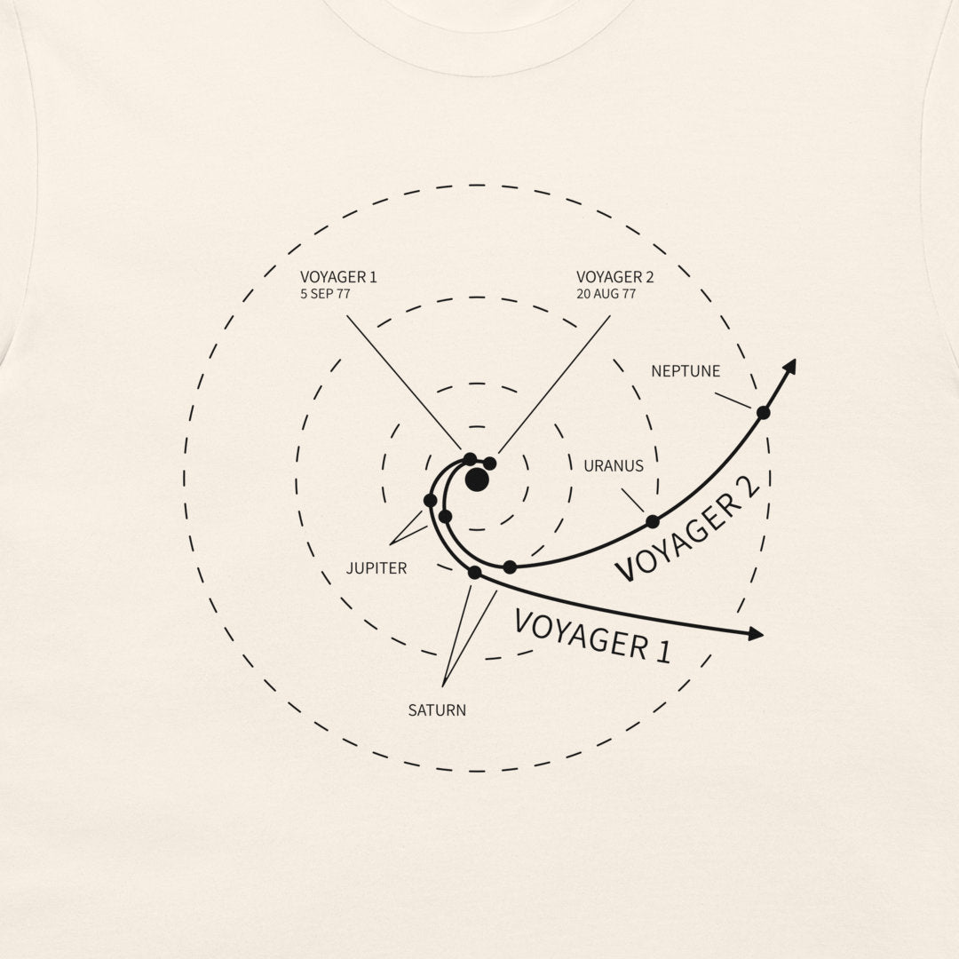 A close-up of a light cream-colored t-shirt featuring a black printed graphic of Voyager 1 and Voyager 2 spacecraft trajectories relative to the solar system planets, including Jupiter, Saturn, Uranus, Neptune, and the Sun.