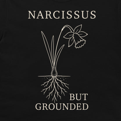 A close-up of a black t-shirt, featuring a white graphic print of a daffodil with its roots exposed and the text 'NARCISSUS BUT GROUNDED' in a serif font.