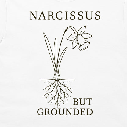 A white t-shirt featuring a dark brown graphic of a narcissus flower with its roots exposed, accompanied by the text 'NARCISSUS BUT GROUNDED'.