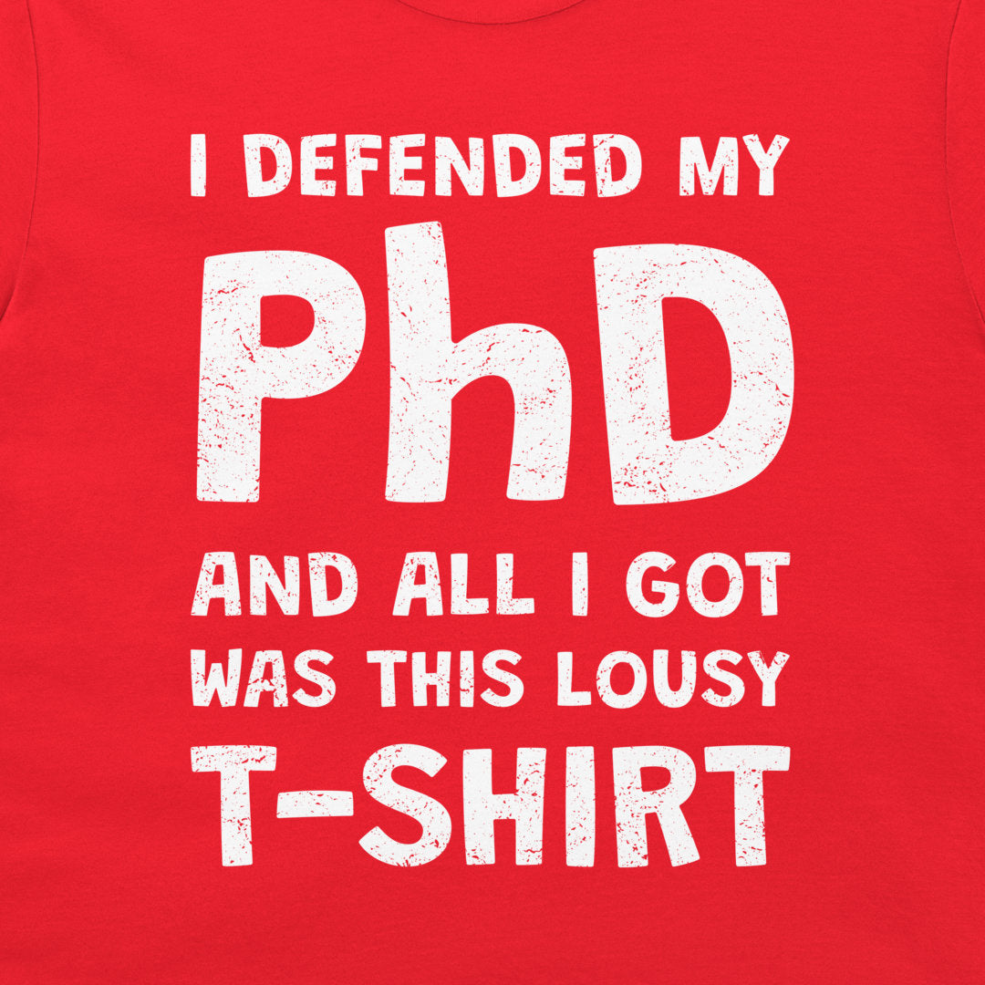 A close-up of a bright red T-shirt with a distressed white graphic text that reads, 'I DEFENDED MY PhD AND ALL I GOT WAS THIS LOUSY T-SHIRT'.
