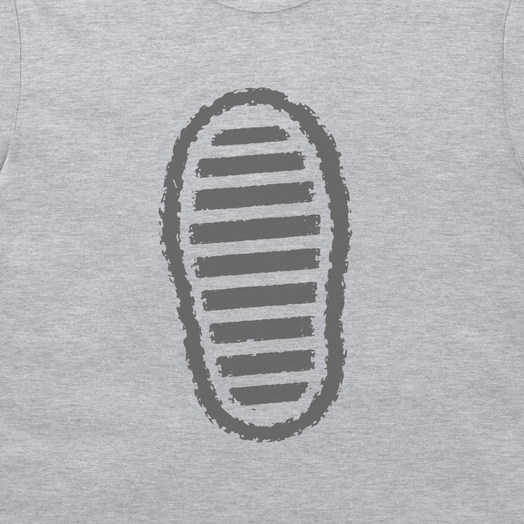 A close-up of a grey t-shirt, featuring a dark grey graphic print of a shoe sole with horizontal stripes.